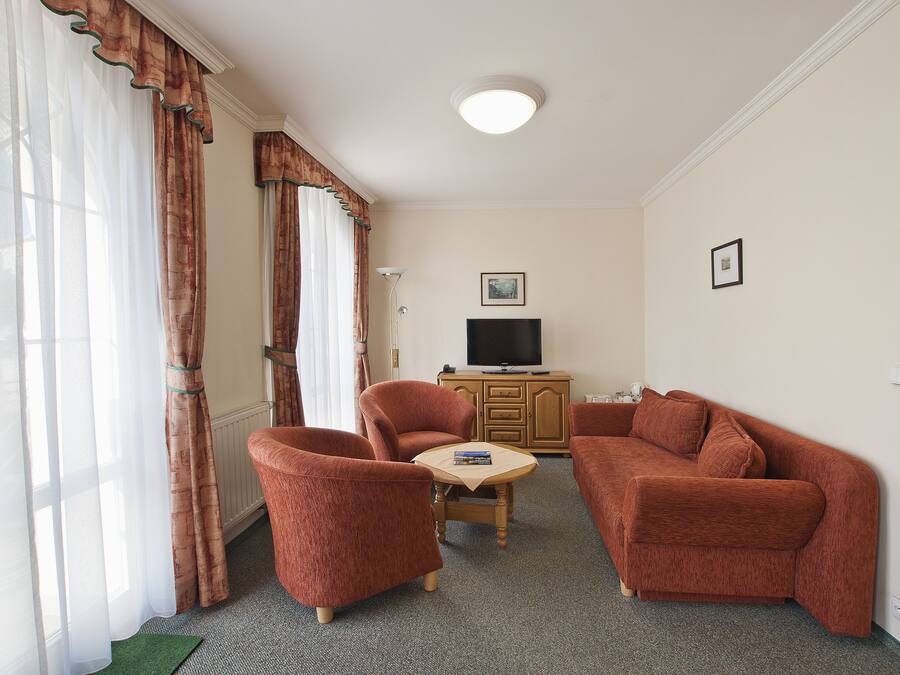 A living room with a sofa, two armchairs, a small table, a television, and a cabinet.