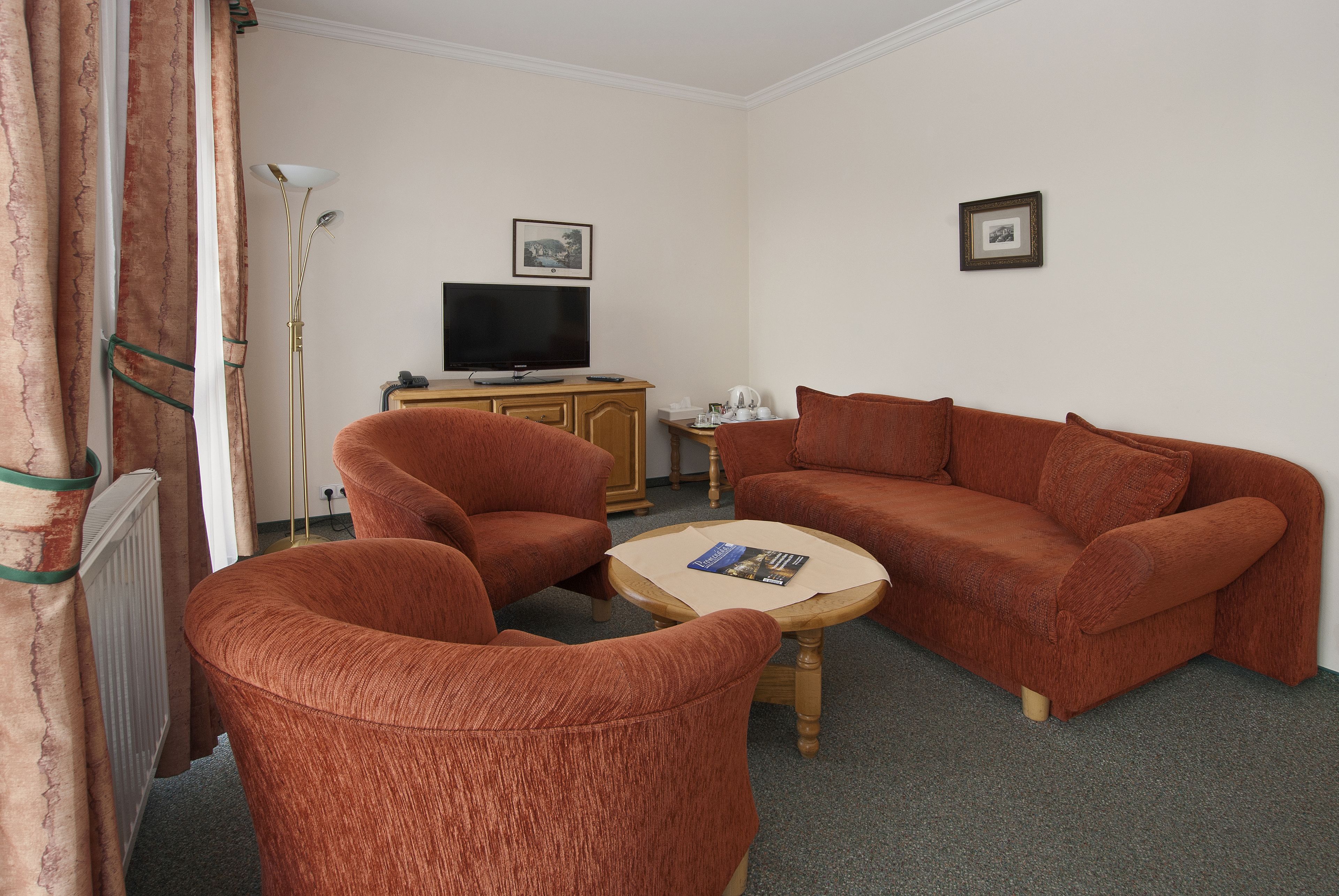 A living room with a sofa, two armchairs, a coffee table, a television, and a radiator.