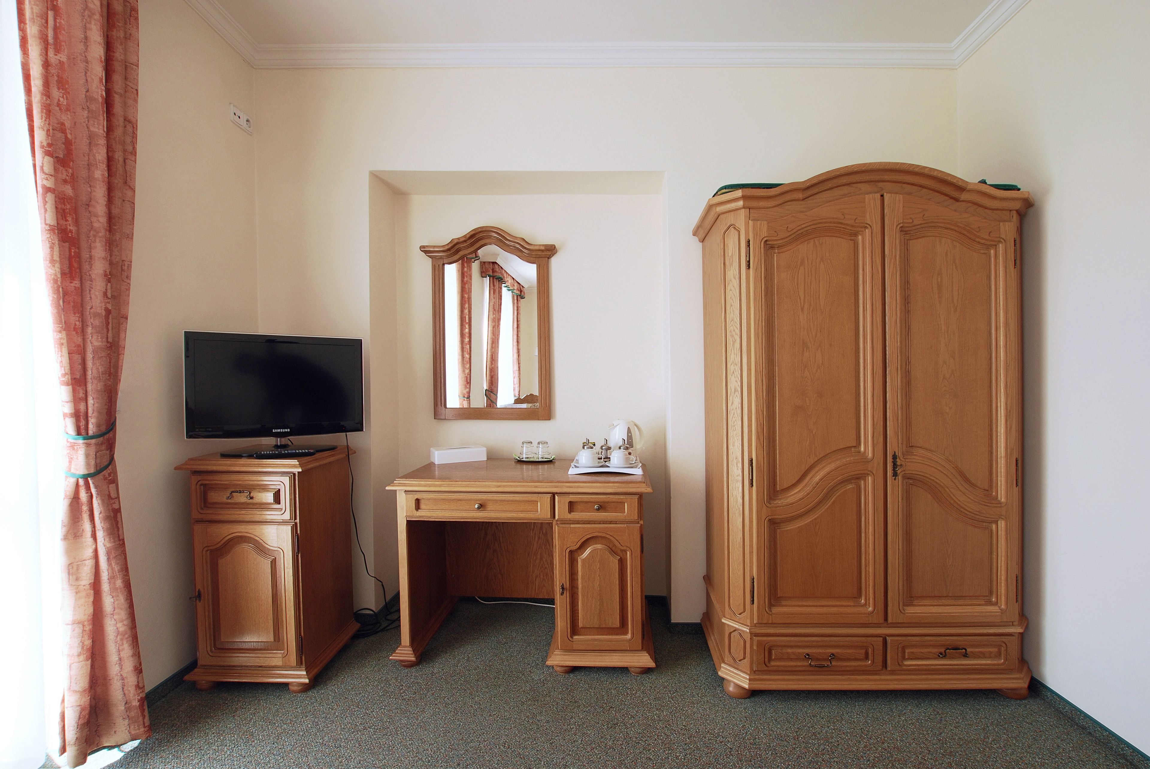 Una habitación con escritorio de madera, televisor, armario y espejo.