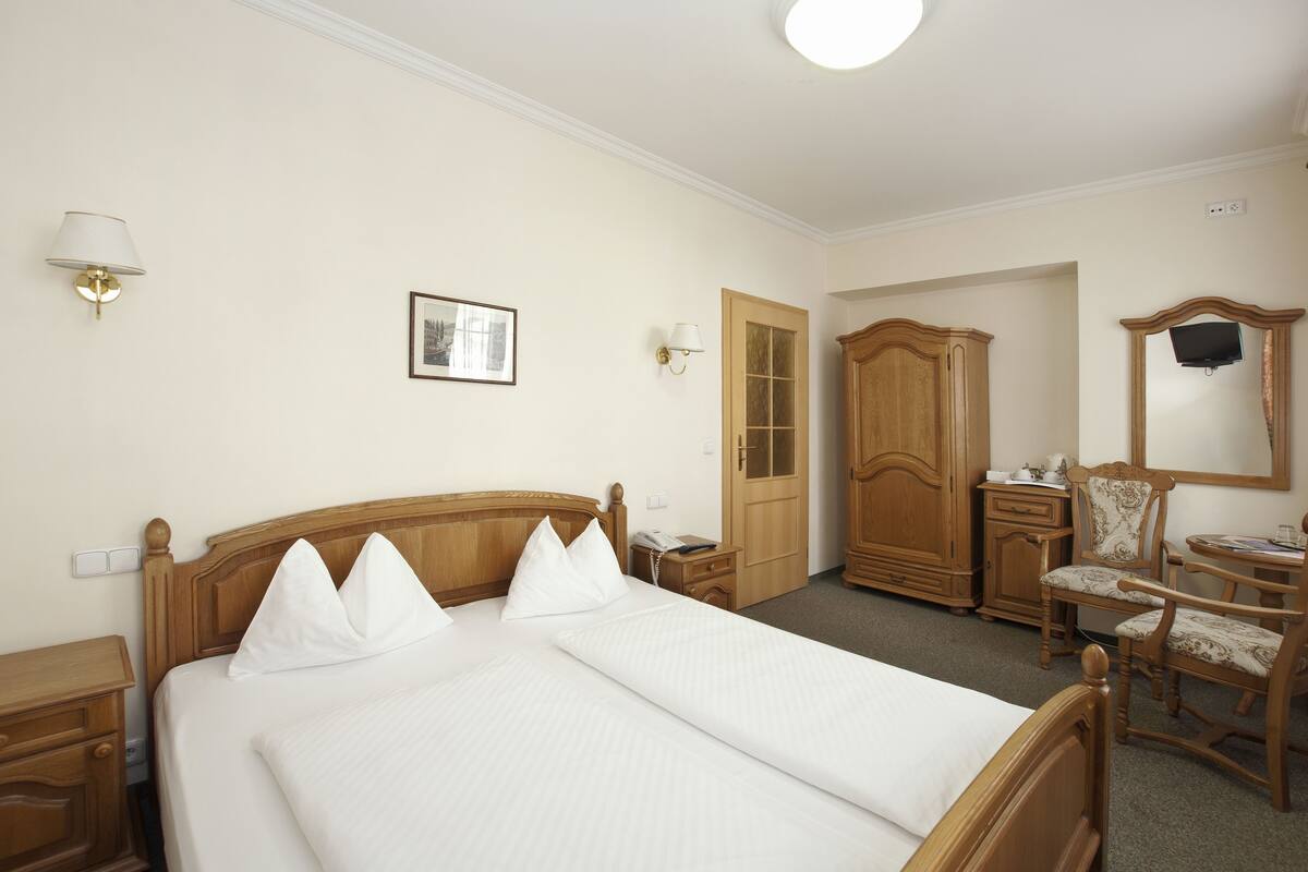 A neatly arranged hotel room with a large bed, wooden furniture, a desk, and a television.