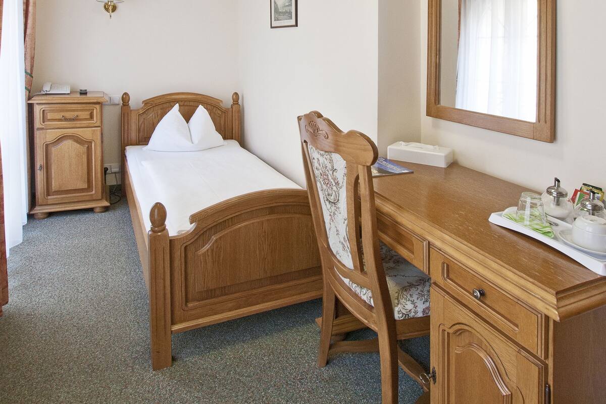 A bedroom with a wooden bed, a desk with a mirror, and a bedside table.