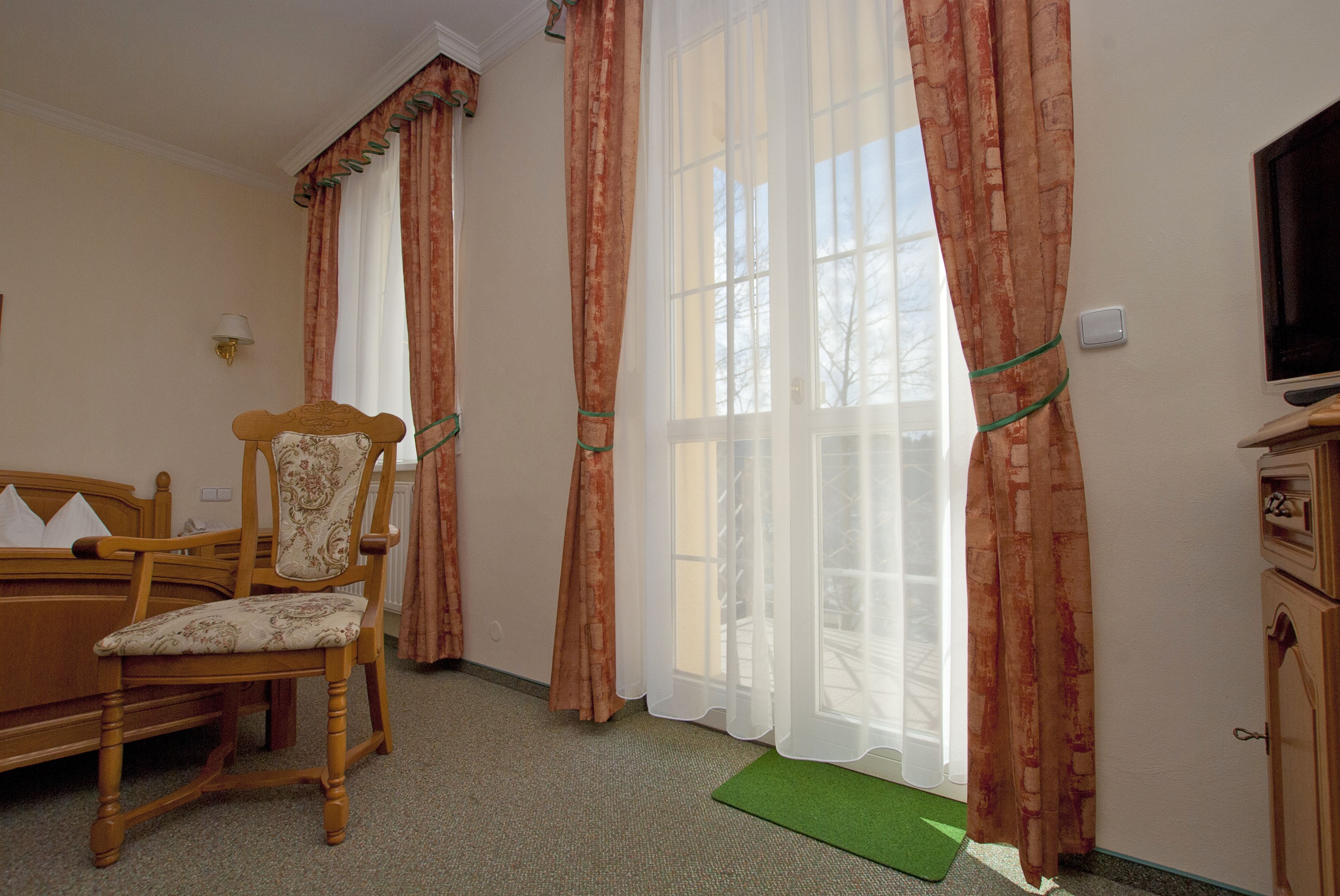 A hotel room with a wooden chair, a desk, and a television.