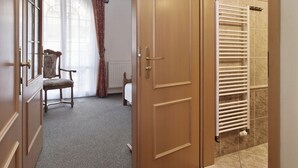 Habitación de hotel con puerta de madera, un radiador, una silla y una ventana con cortinas.