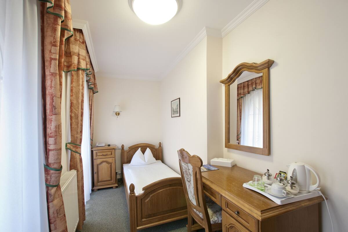 A bedroom with a wooden bed, a wooden desk, a mirror, and a radiator.