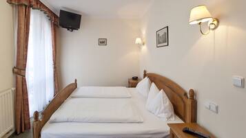 A hotel room with a double bed, a bedside table with a remote control, a wall-mounted TV, and two wall sconces.
