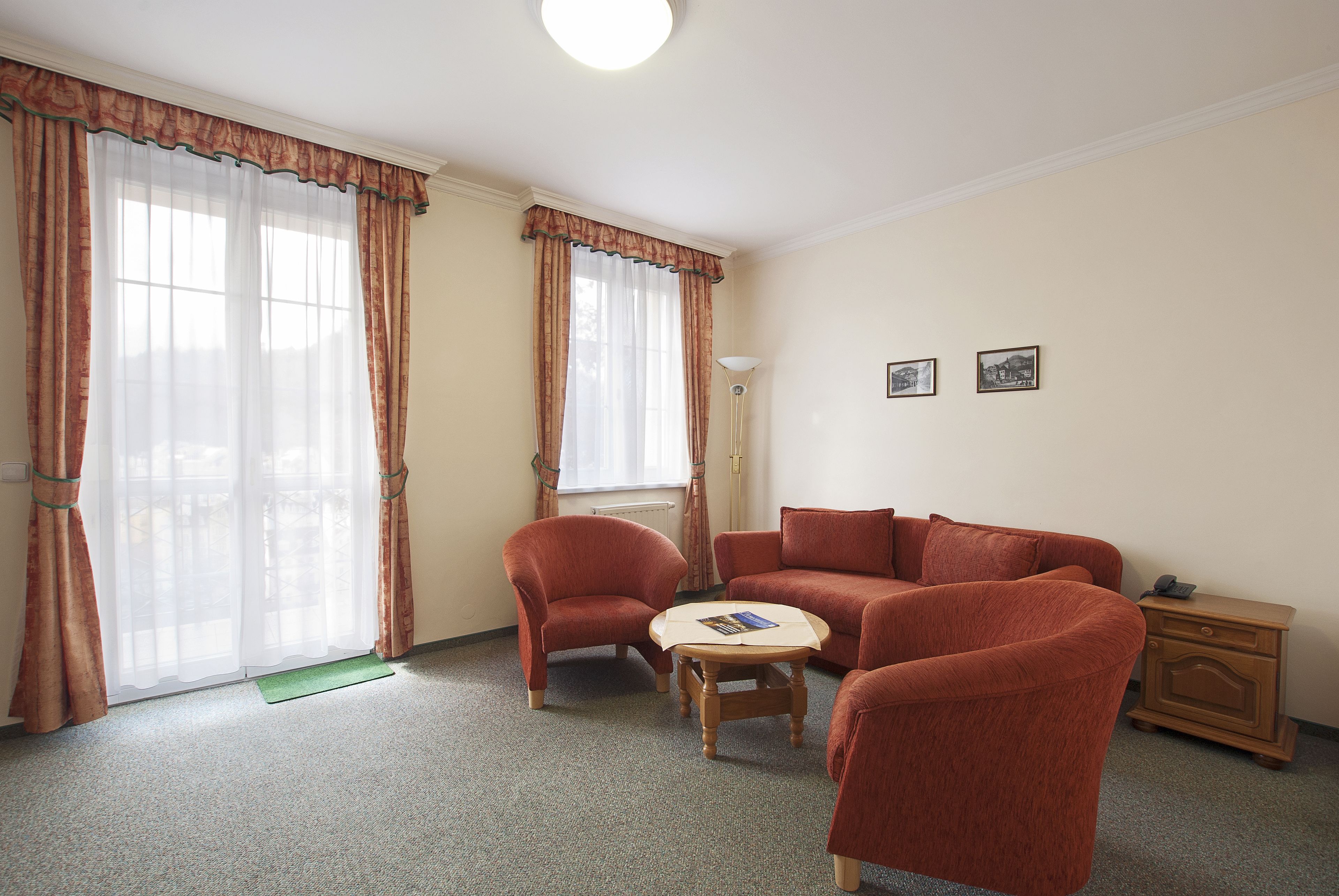 A room with a sofa, two armchairs, a small round table, and a nightstand with a lamp.