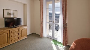 Una habitación con un armario de madera, un televisor de pantalla plana, un ventanal corredero con cortinas y vistas a la ciudad.