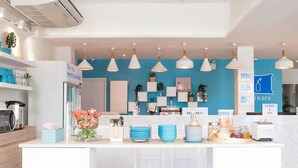 A modern kitchen with a central island, white cabinets, and blue accents. There are hanging pendant lights, a self-service beverage station, and various kitchen appliances. - Me U Hostel Pattaya (Pattaya)
