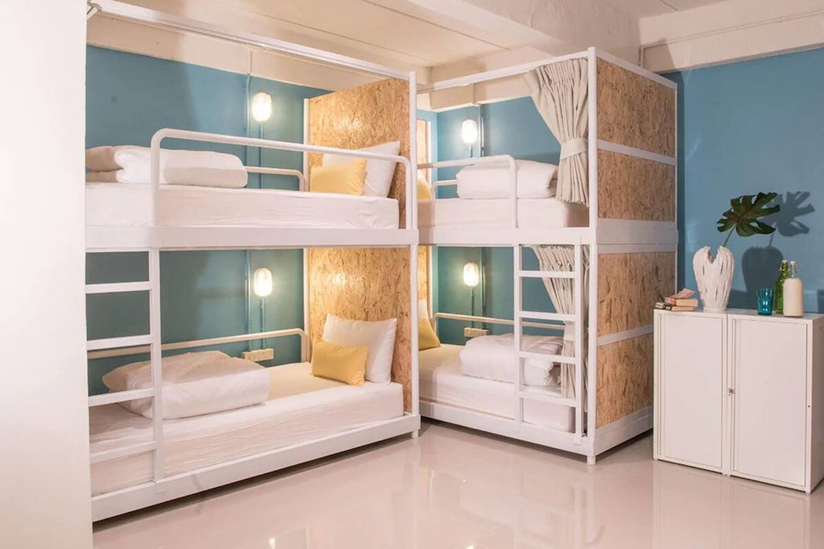 Ein Schlafzimmer mit Etagenbett, blauer Wand, weißer Bettwäsche und einem kleinen Schrank mit Dekoration.