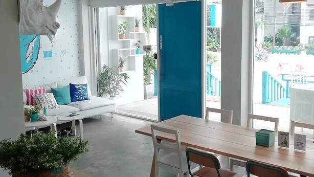 A modern interior with a wooden dining table, chairs, and a blue door leading to an outdoor area. - Me U Hostel Pattaya (Pattaya)