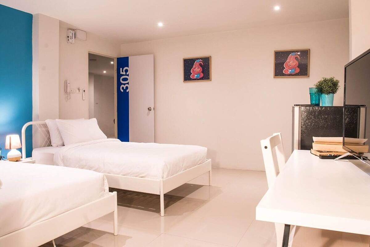 Ein Hotelzimmer mit zwei Betten, einem Schreibtisch, einem Sessel, einem Fernseher und einer Tür mit der Nummer 305.