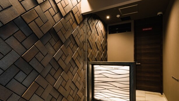 Un interior moderno con una pared de diseño geométrico tipo espiga, una partición de vidrio y suelo de mármol.
