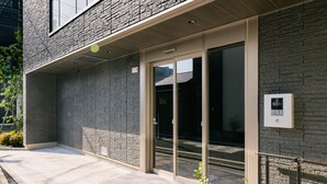 Un edificio con fachada de ladrillo, puertas de cristal grandes y un pequeño espacio exterior con una jardinera.