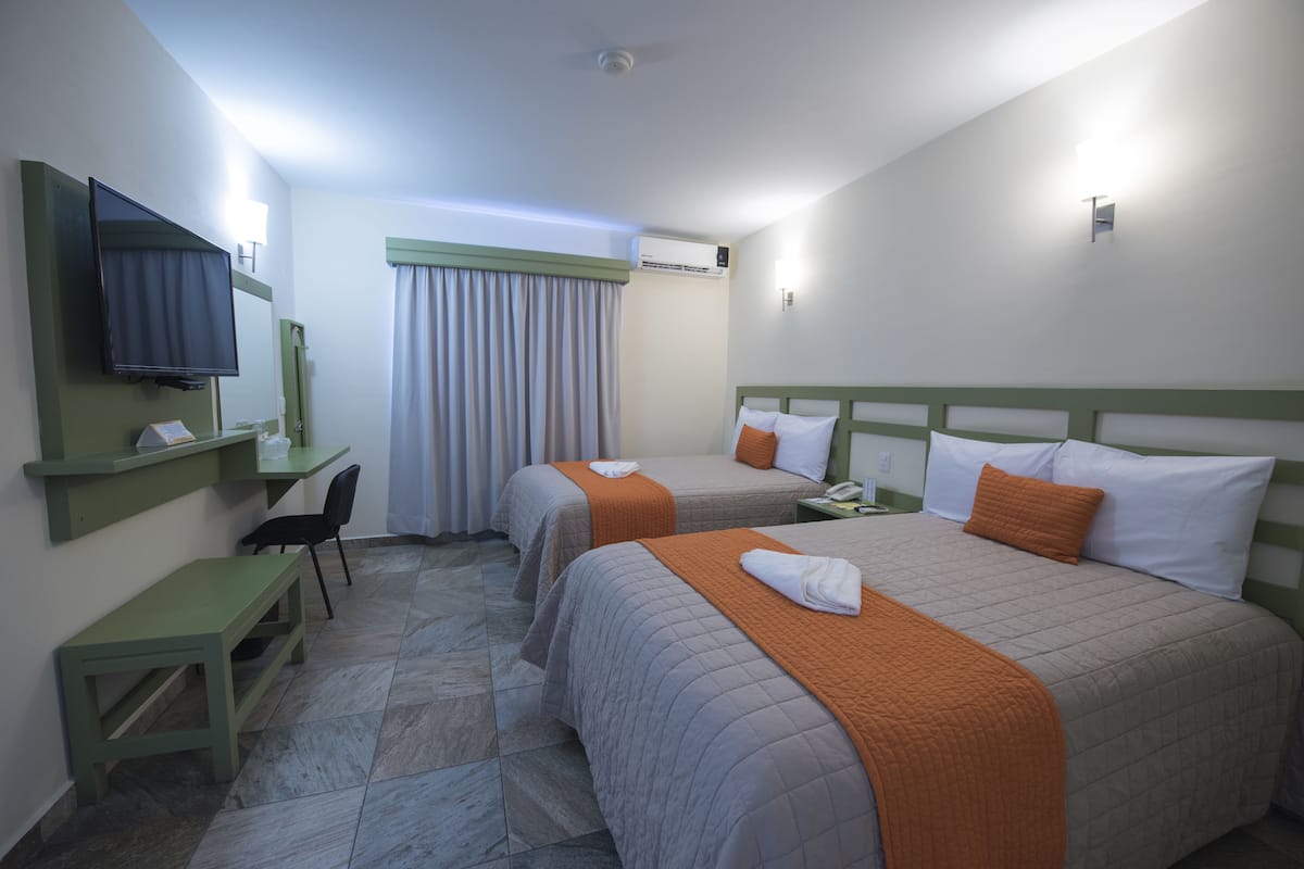 Habitación de hotel con dos camas, un escritorio, una silla, un televisor y un equipo de aire acondicionado.