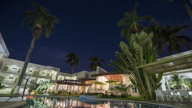 Un hotel con piscina, palmeras y asientos al aire libre.