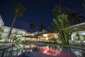 Un hotel con piscina, palmeras y asientos al aire libre.