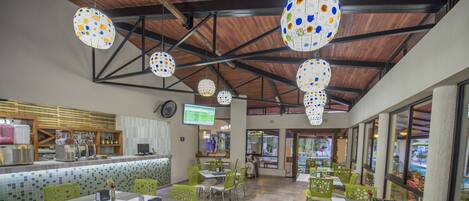 A spacious cafe with green chairs and white tables, a wooden ceiling, and a tiled floor.