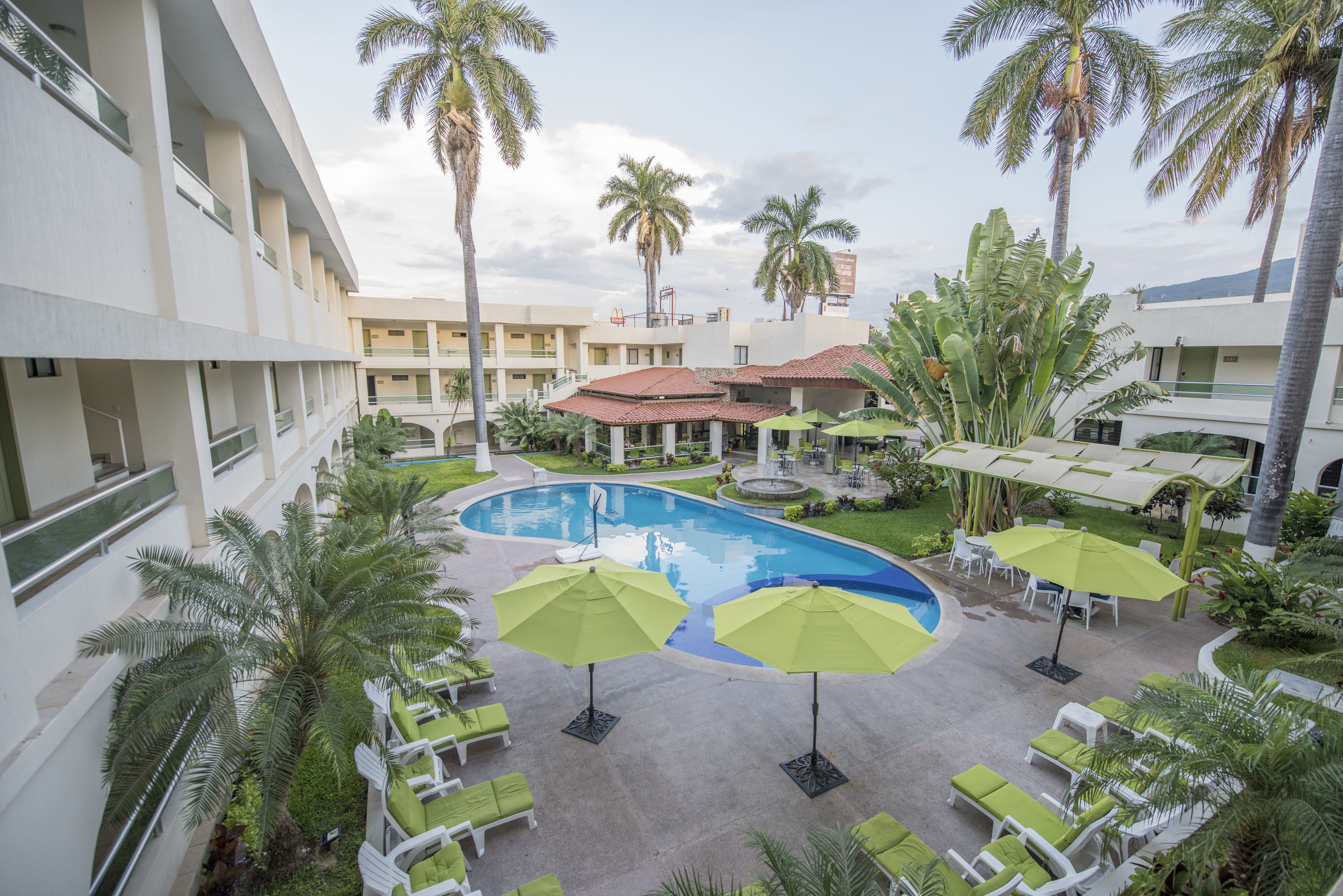 Un patio de hotel con piscina, palmeras y zonas de estar al aire libre.