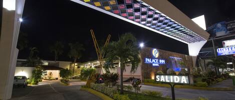 Entrada de un hotel con diseño moderno, un letrero que dice "PALACE INN SALIDA" y un área de estacionamiento visible.