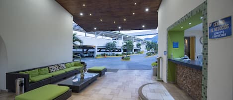 A reception area with a reception desk, a seating area with a sofa and ottoman, and a tiled floor.