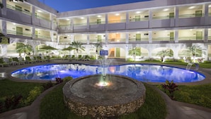 Un hotel de varios pisos con una piscina central, mobiliario exterior y una fuente.