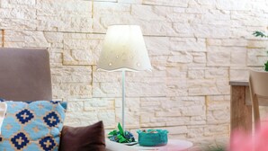 A cozy room with a stone wall, a lamp, a small table with a blue bowl, and a cushion with a geometric pattern. - Cagliari Magica (Cagliari)