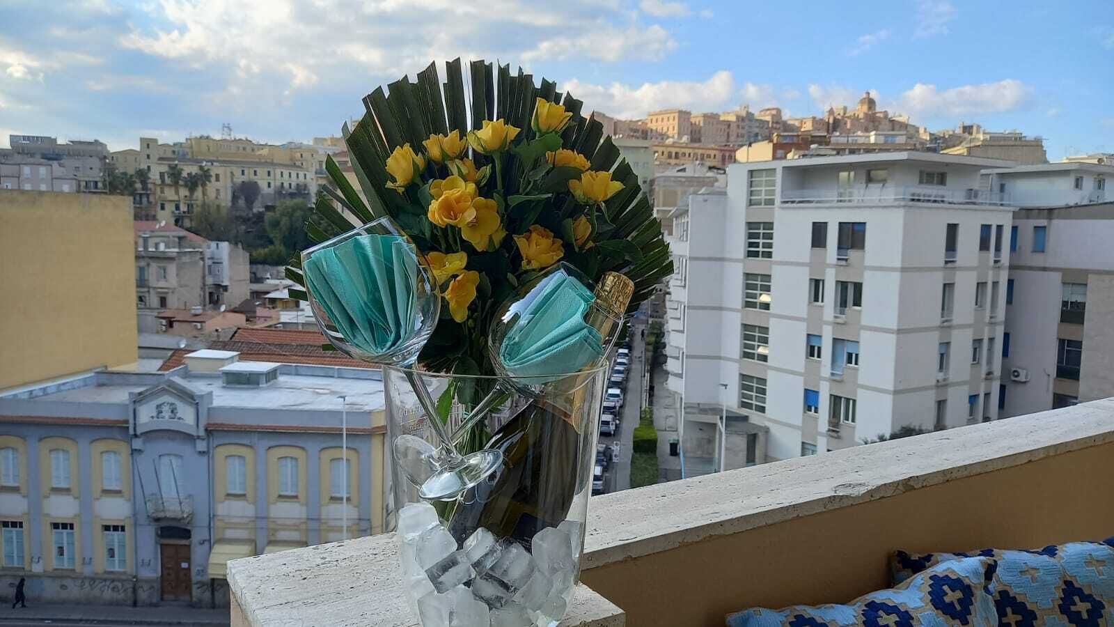 A vase with yellow flowers on a balcony overlooking a cityscape.