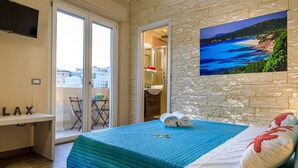 A bedroom with a bed, a TV, a balcony with a table and chairs, and a stone wall with a picture. - Cagliari Magica (Cagliari)