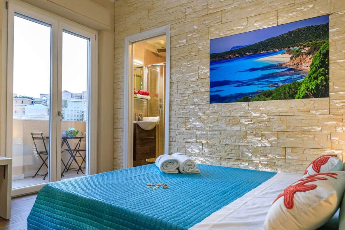 Una camera da letto con un letto, una televisione, un balcone con tavolo e sedie e un muro in pietra con un quadro.