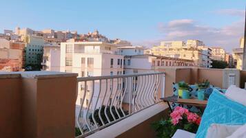 A balcony with a railing, potted plants, and a view of a cityscape with buildings.