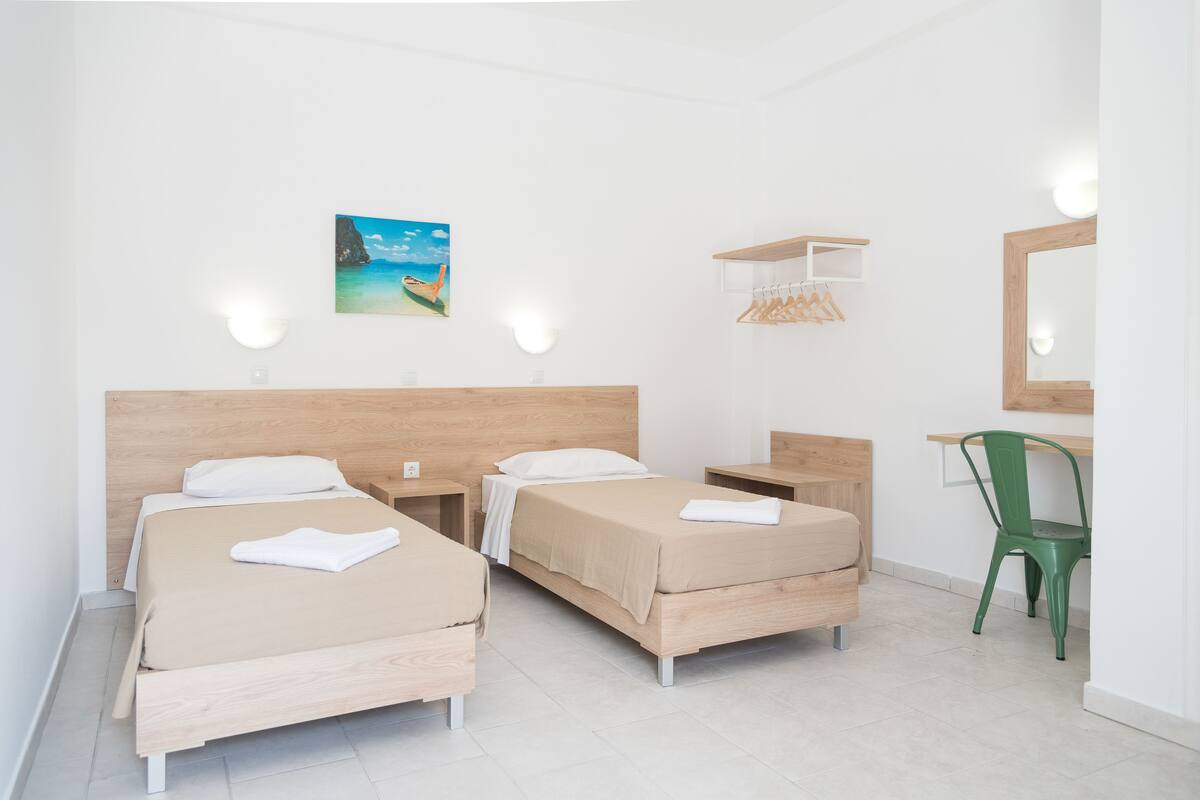 Une chambre d’hôtel avec deux lits, un bureau, une chaise et un tableau au mur.