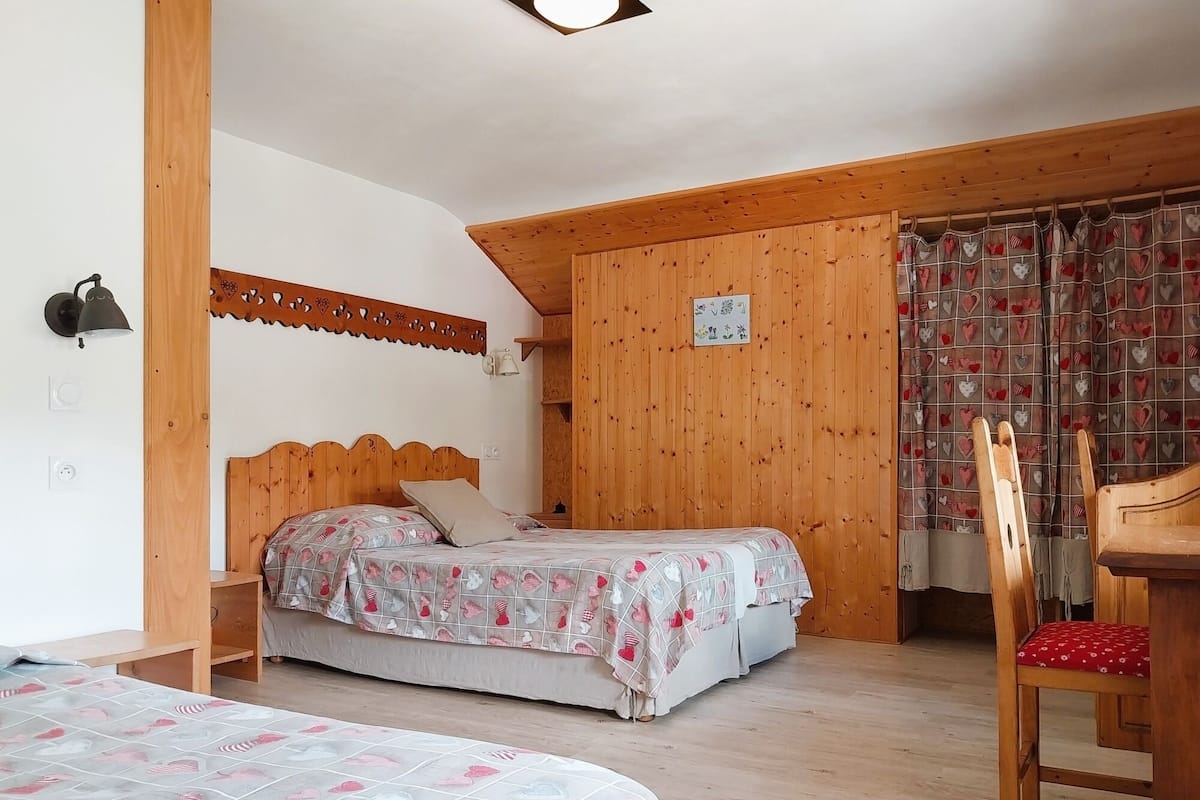 A bedroom with a wooden headboard bed, a wooden chair, a small table, and a patterned curtain.