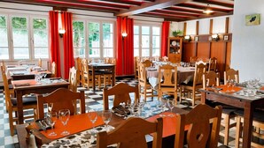 Un restaurante con mesas y sillas de madera, cortinas rojas y piso a cuadros.