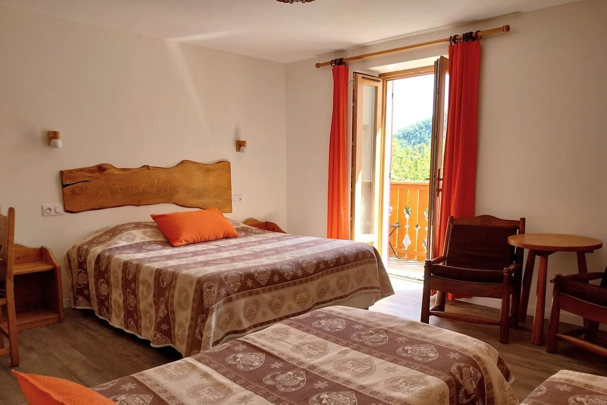 A bedroom with two beds, a wooden headboard, a balcony with red curtains, and a small table.