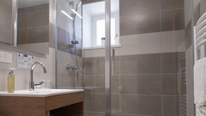 Un baño con cabina de ducha de vidrio, lavamanos con espejo y toallero.