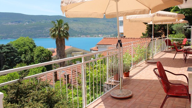 A balcony with outdoor furniture, a view of the sea, and a mountainous landscape. - Guest House Tomanovic (Herceg Novi)