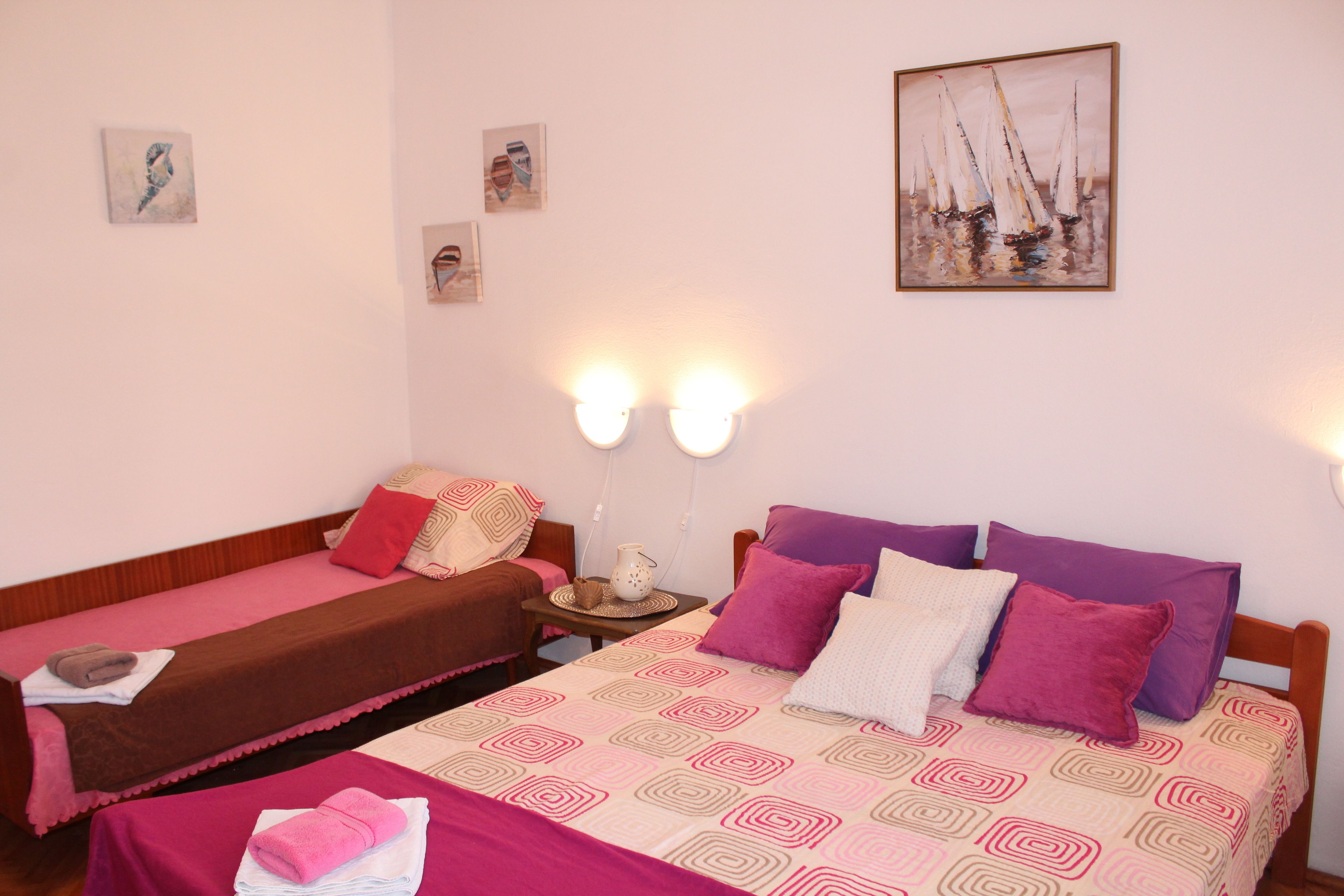 Una habitación con dos camas individuales, una cama grande con ropa de cama estampada, y un cuadro con barcos a vela en la pared.