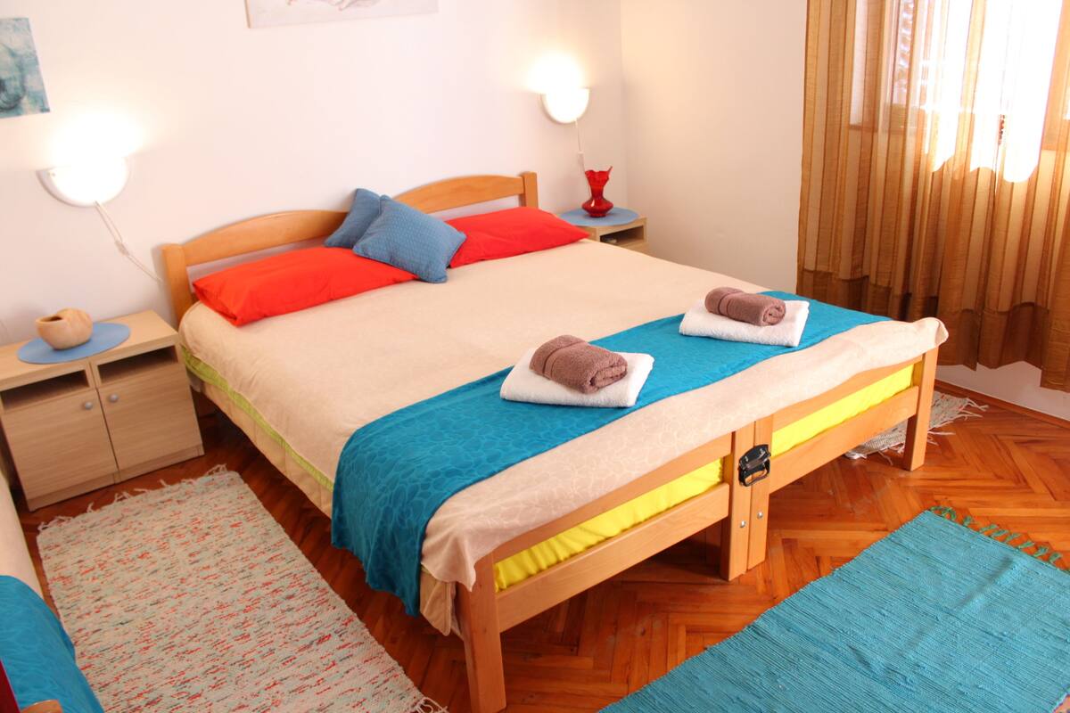Une chambre à coucher bien rangée, avec un lit en bois, deux tables de chevet, une commode et une fenêtre avec des rideaux.