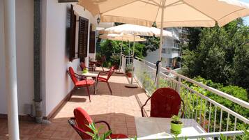 Un balcon avec des chaises rouges, une table et un pot de fleurs.