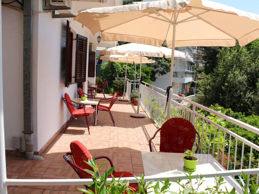 Un balcon avec des chaises rouges, une table et un pot de fleurs.