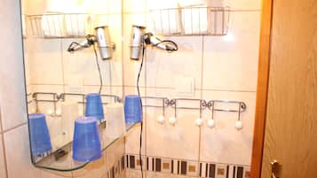 Une salle de bain équipée d’un miroir, de sèche-cheveux et d’un présentoir avec des tasses et des bouteilles.