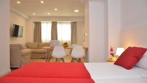 A hotel room with a bed, a desk with a laptop, a TV, and a seating area with chairs. - Bet Apartments - Abastos (Valencia)