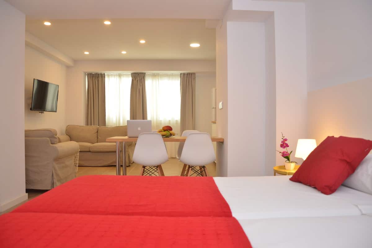 A hotel room with a bed, a desk with a laptop, a TV, and a seating area with chairs.