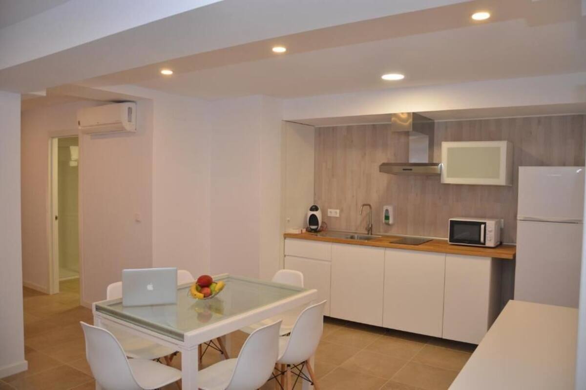 A modern kitchen with white cabinets, a microwave, and a built-in oven. There is a glass dining table with chairs and a laptop.