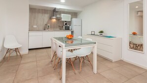 A modern kitchen with white cabinetry, a glass-top dining table, and a small island with a plant. - Bet Apartments - Abastos (Valencia)