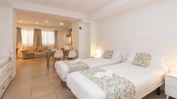 Habitación de hotel con dos camas, un sofá, una mesa de comedor y una pequeña cocina.
