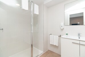 Un baño moderno con cabina de ducha de vidrio, un lavabo blanco y un espejo sobre el lavabo.