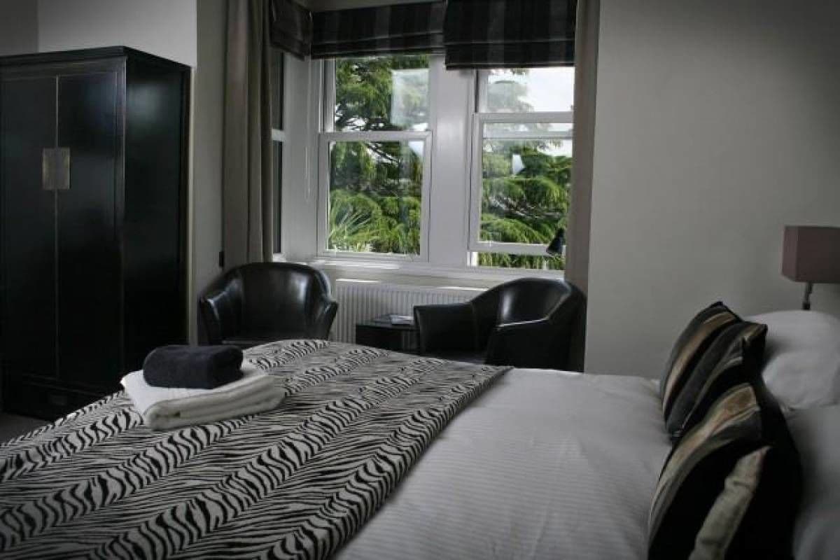 A hotel room with a bed, a wardrobe, a window with a view of greenery, and a desk with a chair.