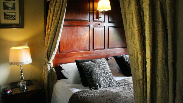 Une chambre à coucher avec une tête de lit en bois, une lampe de chevet et un lit agrémenté d’oreillers à motifs.