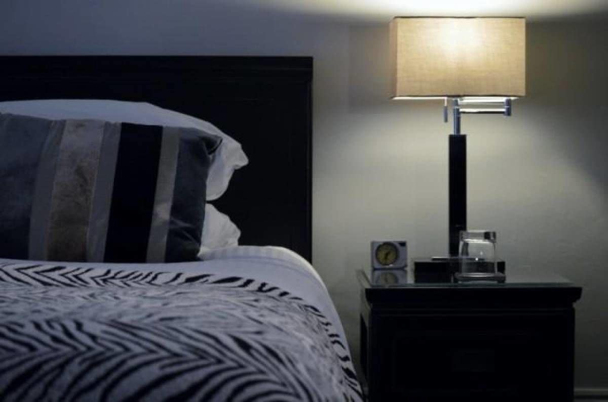 Um quarto com cama, mesa de cabeceira, abajur e relógio.